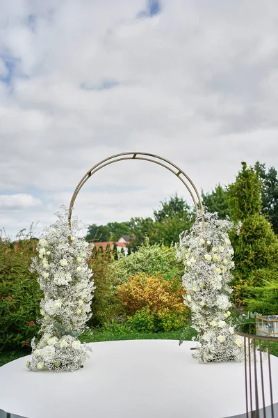 The welcoming arch is decorated with white flowers and roses. Wedding celebration ceremony.