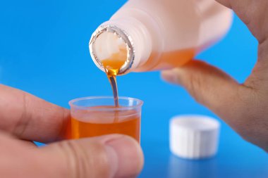 Tıbbi şurup, mavi arka planda sıvı hacim bölümleri olan bir kaba dökülür. Hastalıkların tedavisi ve önlenmesi. Bağışıklığı güçlendiriyor.