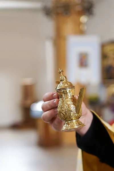The priest holds a cup of holy water in his hands for the rite of baptism of a newborn.