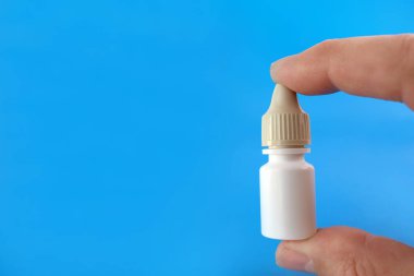 Bir adam mavi arka planda elinde damlalar şeklinde bir ilaç şişesi tutuyor..