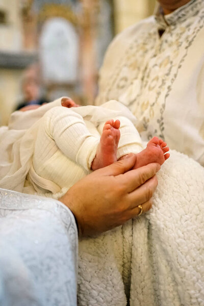 The legs of a newborn during church baptism.