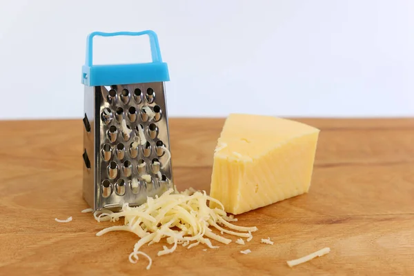 A miniature grater and a piece of cheese on a wooden board.