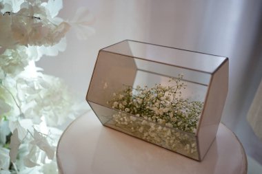 Masanın üzerinde tebrik kartları için çiçekli şeffaf bir kutu var..                               