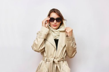 Güneş gözlüklü güzel bir kız hafif bir sonbahar yağmurluğu ve eşarp giyer..