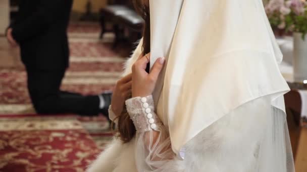 教会の結婚式では 花嫁はアイコンの前に祈り 彼女の頭にスカーフで膝の上に立っています 教会の結婚式の伝統 — ストック動画