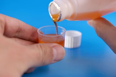 Tıbbi şurup, mavi arka planda sıvı hacim bölümleri olan bir kaba dökülür. Hastalıkların tedavisi ve önlenmesi. Bağışıklığı güçlendiriyor.