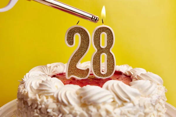 A candle in the form of the number 28, stuck in a festive cake, is lit. Celebrating a birthday or a landmark event. The climax of the celebration.