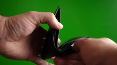 Bir adam yeşil arka planda bir cüzdanda dolar sayar.