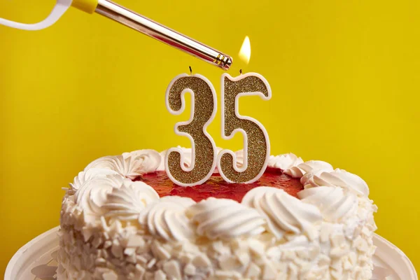 A candle in the form of the number 35, stuck in a festive cake, is lit. Celebrating a birthday or a landmark event. The climax of the celebration.