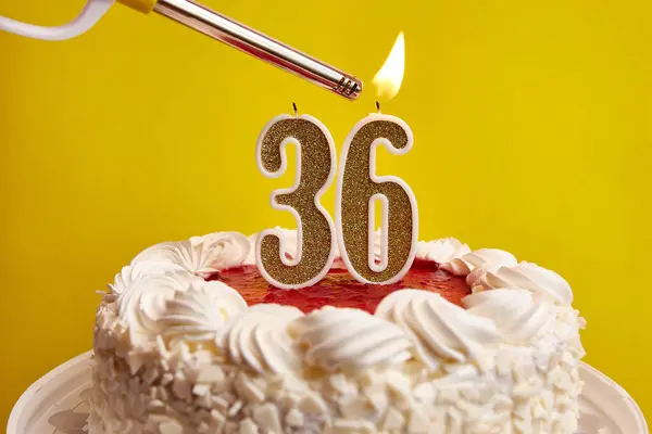 A candle in the form of the number 36, stuck in a festive cake, is lit. Celebrating a birthday or a landmark event. The climax of the celebration.