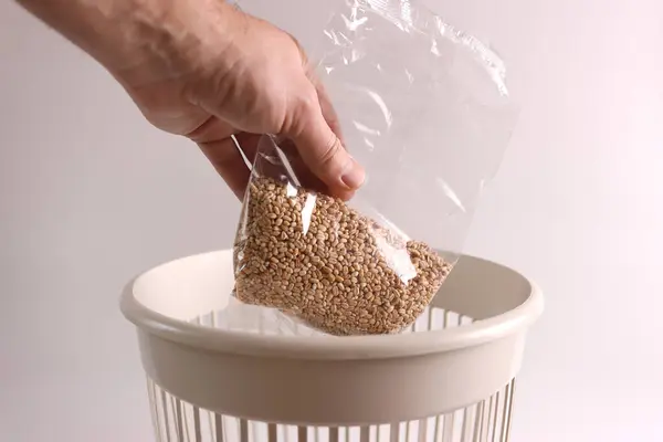 A bag of expired grain is thrown into the bin for recycling