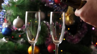 Parıldayan çelenkleri olan bir Noel ağacının arka planına şampanya bardaklara dökülüyor. Yavaş çekim.