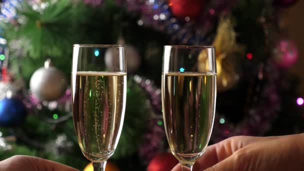 バックグラウンドでは ツインリングガーランドのクリスマスツリーがシャンパンのグラスでトーストを提供しています スローモーション — ストック動画