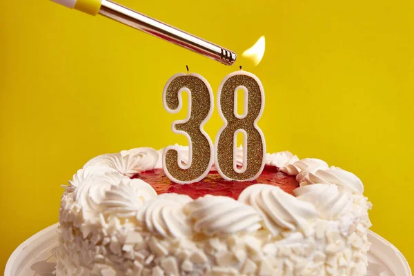 A candle in the form of the number 38, stuck in a festive cake, is lit. Celebrating a birthday or a landmark event. The climax of the celebration.