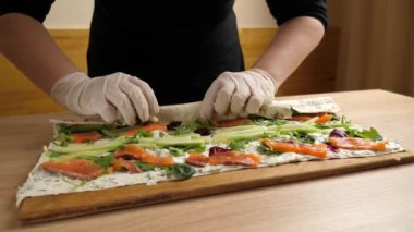 Pide ekmeğini sarıp bir rulo oluşturuyoruz. Peynirli, balıklı ve sebzeli rulo hazırlama. Yavaş çekim.