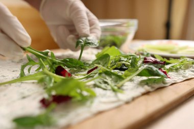 Yeşiller peynirli pide ekmeğine ilave edilir. Peynirli, balıklı ve sebzeli rulo hazırlama