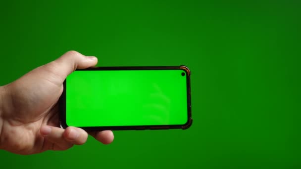 緑色の画面を持つスマートフォンは 緑色の背景に手元に水平に保持されます — ストック動画