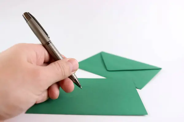 Green envelope, sheet of paper and pen in hand on white background.