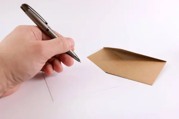 Brown envelope, sheet of paper and pen in hand on white background.