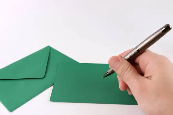 Green envelope, sheet of paper and pen in hand on white background.