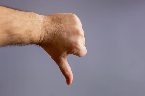 Человеческая рука показывает большие пальцы вниз (плохой) жест на сером фоне.