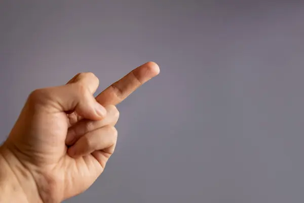 Hand gesture with middle finger on gray background.