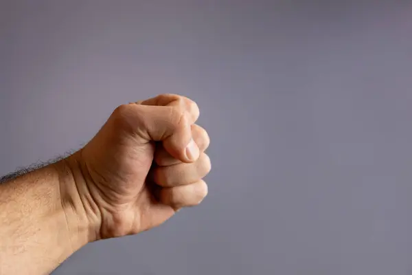 Male hand clenched into a fist on a gray background.