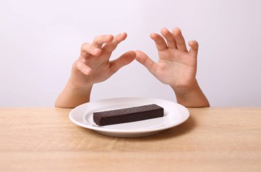 A child's hands are visible from under the table, trying to take a chocolate wafer from the table. clipart