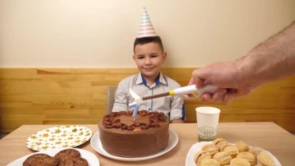 少年はお祝いのケーキを持ってテーブルの前に座っており そこでは7という数字の形でろうそくが燃えている 誕生日のお祝いコンセプト — ストック動画