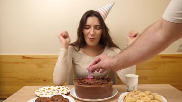 女の子がお祝いのケーキを持ってテーブルの前に座り その中に16という数字の形をしたろうそくが立ち往生している 誕生日のお祝いのコンセプト — ストック動画