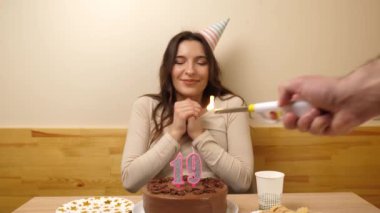 Kız elinde şenlikli bir pastayla bir masanın önünde oturuyor, 19 numara şeklinde bir mum yanıyor ve o da söndürüyor. Doğum günü kutlaması konsepti.