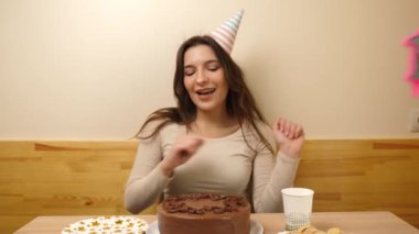 Bir kız elinde şenlikli bir pastayla masanın önünde oturuyor. 18 numaralı pastaya mum takılmış. Doğum günü kutlaması konsepti.