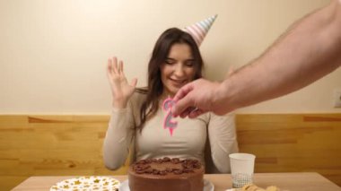 Bir kız elinde şenlikli bir pastayla masanın önünde oturuyor. 21 numaralı pastaya bir mum takılmış. Doğum günü kutlaması konsepti.