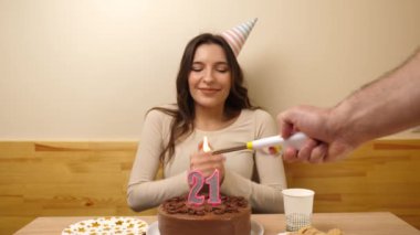 Kız elinde şenlikli bir pastayla bir masanın önünde oturuyor. 21 numara şeklinde bir mum yanıyor ve söndürüyor. Doğum günü kutlaması konsepti.