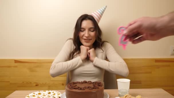 女の子がお祝いのケーキを持ってテーブルの前に座っていて 20という数字の形をしたろうそくが立ち往生している 誕生日のお祝いのコンセプト — ストック動画