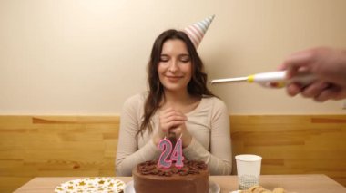 Kız elinde şenlikli bir pastayla bir masanın önünde oturuyor, içinde 24 numara şeklinde bir mum yanıyor ve söndürüyor. Doğum günü kutlaması konsepti.