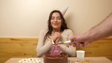 Kız elinde şenlikli bir pastayla bir masanın önünde oturuyor, içinde 25 numara şeklinde bir mum yanıyor ve söndürüyor. Doğum günü kutlaması konsepti.