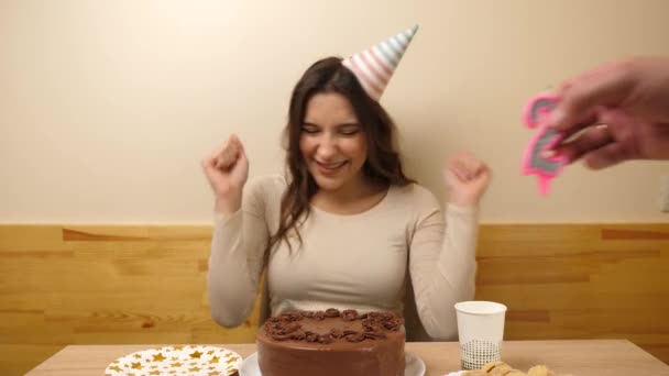 一个女孩坐在桌前 手里拿着一个喜庆的蛋糕 上面插着一支24号的蜡烛 庆祝生日的概念 — 图库视频影像