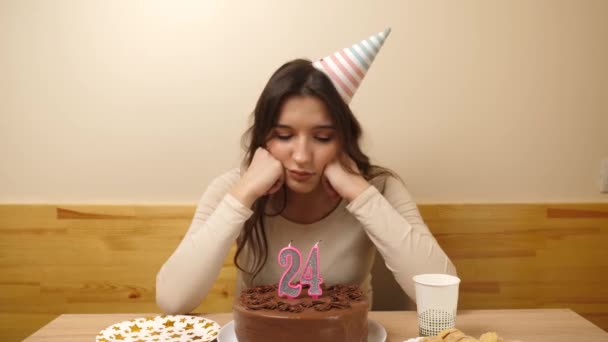 一个心烦意乱的女孩坐在餐桌前 手里拿着一个喜庆的蛋糕 桌上插着一支24号的蜡烛 生日的概念 — 图库视频影像