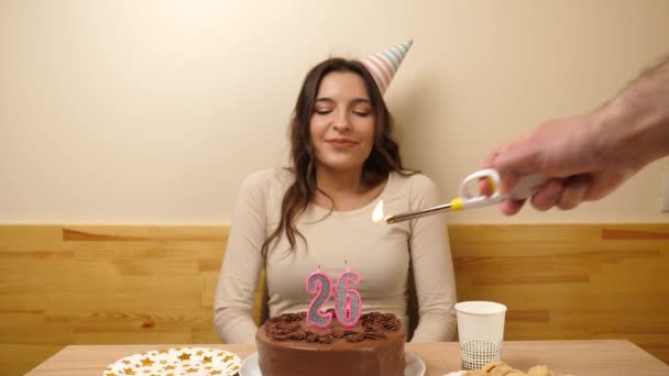 女の子は 26という数字の形をしたろうそくが燃えているお祝いのケーキでテーブルの前に座っており 彼女は吹き出します 誕生日のお祝いコンセプト — ストック動画