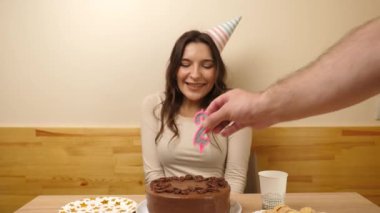 Bir kız elinde şenlikli bir pastayla masanın önünde oturuyor. 28 numaralı pastaya mum takılmış. Doğum günü kutlaması konsepti.