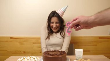 Bir kız elinde şenlikli bir pastayla bir masanın önünde oturuyor, 27 numara şeklinde bir mumla. Doğum günü kutlaması konsepti.