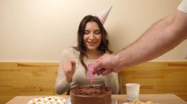 Bir kız elinde şenlikli bir pastayla bir masanın önünde oturuyor ve 29 numaralı pastaya bir mum sıkışıyor. Doğum günü kutlaması konsepti.