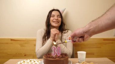 Kız elinde şenlikli bir pastayla bir masanın önünde oturuyor, içinde 30 numara şeklinde bir mum yanıyor ve söndürüyor. Doğum günü kutlaması konsepti.