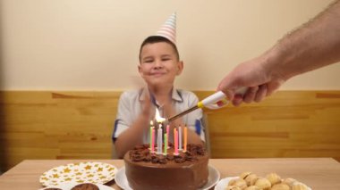 Çocuk elinde şenlikli bir pasta ve mumla bir masanın önünde oturur, onları söndürür ve hediyeler alır. Doğum günü kutlaması konsepti.