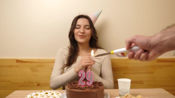 女の子はお祝いのケーキを持ってテーブルの前に座っており 29という数字の形でろうそくが燃えている 誕生日のお祝いコンセプト — ストック動画
