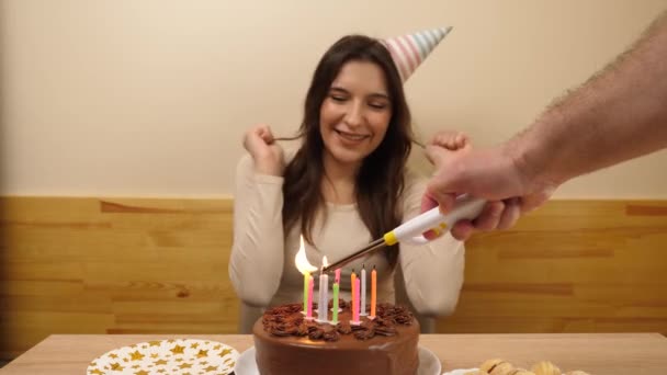 女の子はお祝いのケーキとろうそくでテーブルの前に座り それらを吹き飛ばし 贈り物を受け取ります 誕生日のお祝いコンセプト — ストック動画