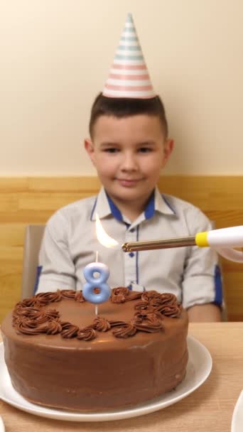 男孩坐在桌前 手里拿着一个喜庆的蛋糕 里面燃着一支八号的蜡烛 他把它吹灭了 生日庆祝的概念 垂直录像 — 图库视频影像