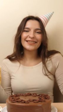 Masanın önünde elinde şenlikli bir pastayla oturan bir kız. 17 numaralı pastaya mum takılmış. Doğum günü kutlaması konsepti. dikey video
