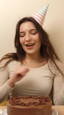 Bir kız elinde şenlikli bir pastayla masanın önünde oturuyor. 18 numaralı pastaya mum takılmış. Doğum günü kutlaması konsepti. dikey video